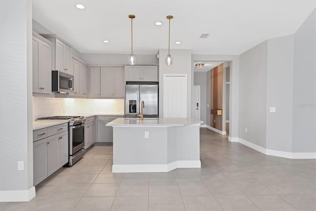 kitchen with light tile patterned flooring, gray cabinetry, an island with sink, pendant lighting, and stainless steel appliances