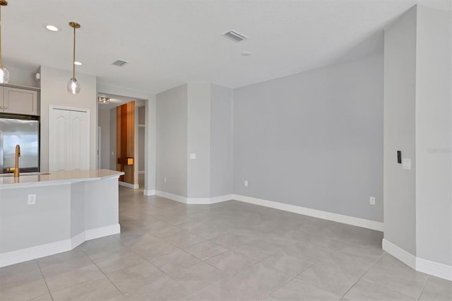 kitchen with stainless steel refrigerator, sink, hanging light fixtures, and light tile patterned floors