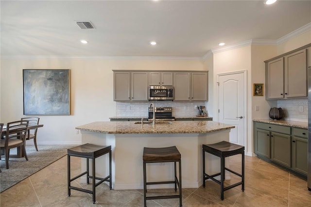 kitchen featuring stainless steel appliances, a center island with sink, sink, light stone countertops, and a kitchen bar