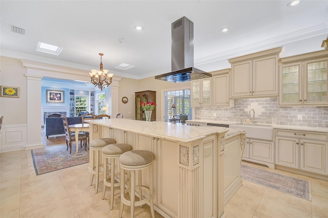 kitchen with island exhaust hood, a kitchen island, cream cabinetry, hanging light fixtures, and sink