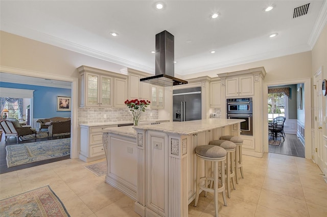 kitchen with island range hood, appliances with stainless steel finishes, a center island, and cream cabinets