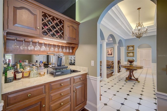 bar with a notable chandelier, ornamental molding, decorative light fixtures, and ornate columns