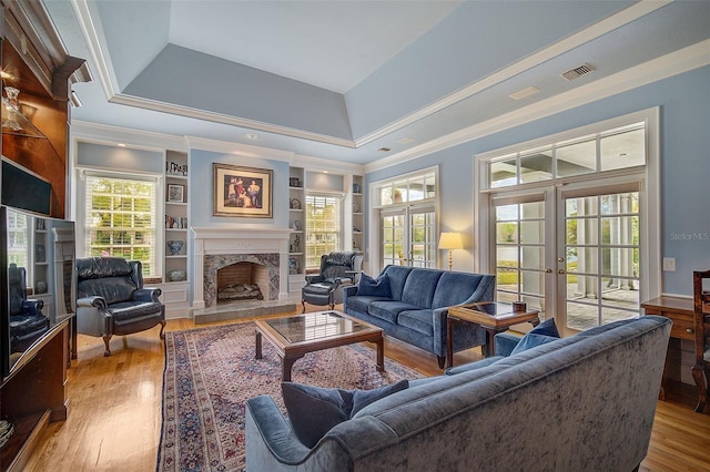 living room featuring a tray ceiling, light wood-type flooring, crown molding, a fireplace, and french doors