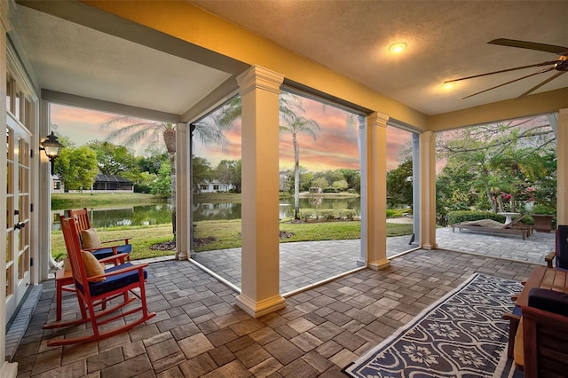 sunroom featuring ornate columns, a healthy amount of sunlight, a water view, and ceiling fan