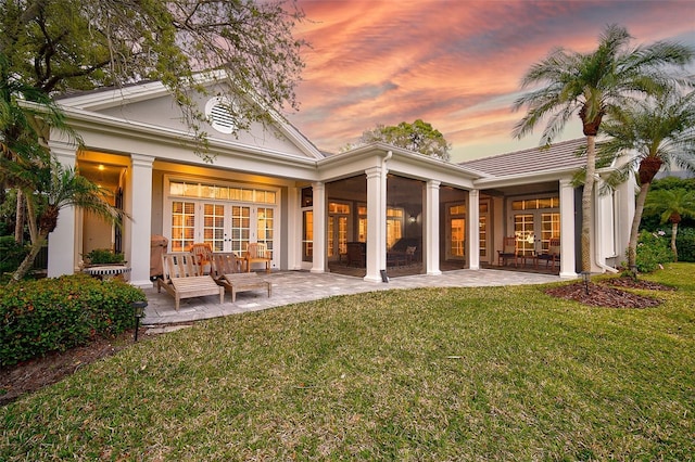 back house at dusk with a patio area, french doors, and a lawn