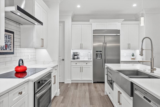 kitchen featuring white cabinets, stainless steel appliances, wall chimney range hood, and backsplash