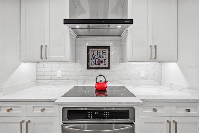 kitchen featuring light stone counters, stainless steel oven, wall chimney exhaust hood, and white cabinets