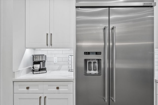 kitchen featuring white cabinets, built in refrigerator, light stone counters, and tasteful backsplash