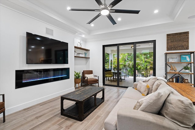 living room with ceiling fan, light wood-type flooring, ornamental molding, and a tray ceiling