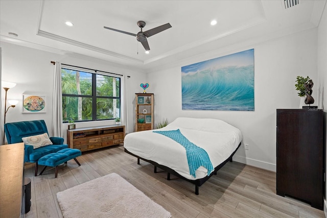 bedroom with ceiling fan, light wood-type flooring, ornamental molding, and a raised ceiling