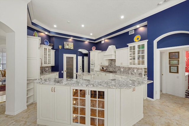 kitchen featuring a large island, white cabinetry, ornamental molding, and light stone countertops