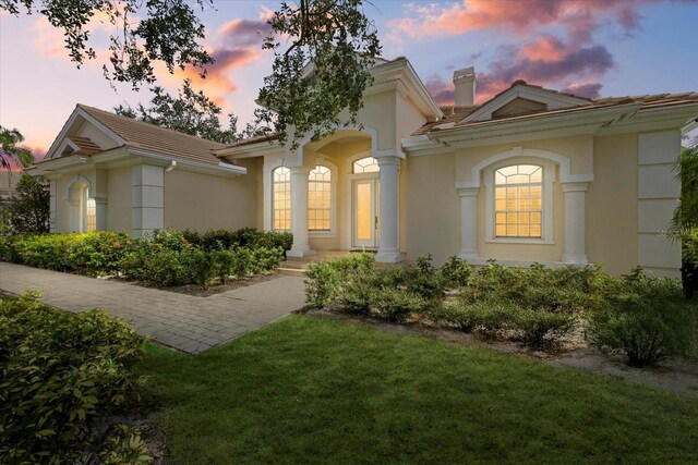 mediterranean / spanish house with a yard, a tiled roof, a chimney, and stucco siding