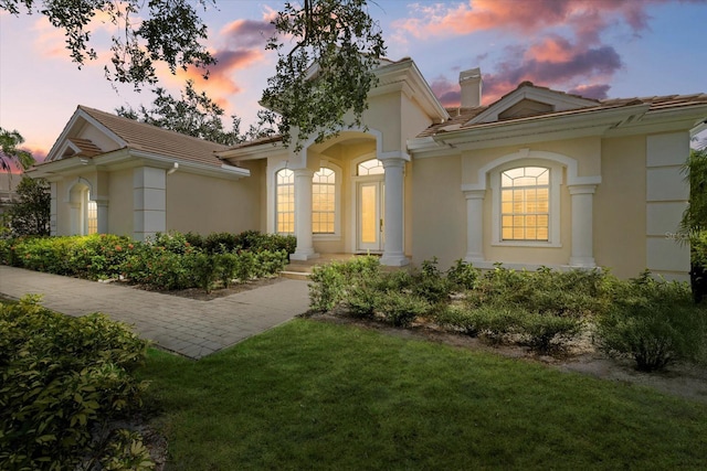 mediterranean / spanish-style house with a tiled roof, a lawn, a chimney, and stucco siding