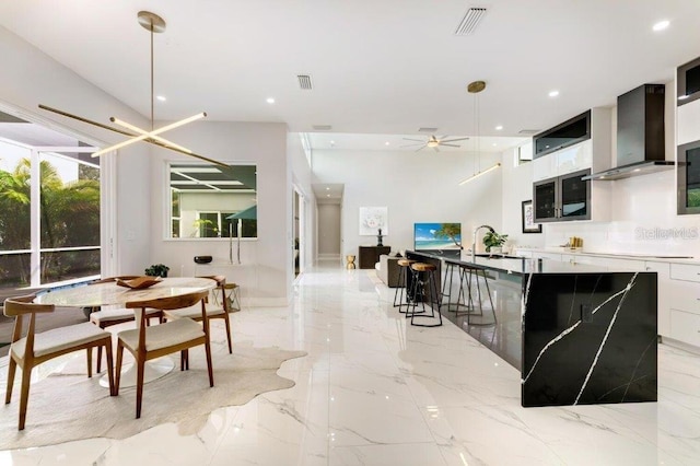 kitchen featuring wall chimney range hood, a breakfast bar area, decorative light fixtures, white cabinets, and ceiling fan