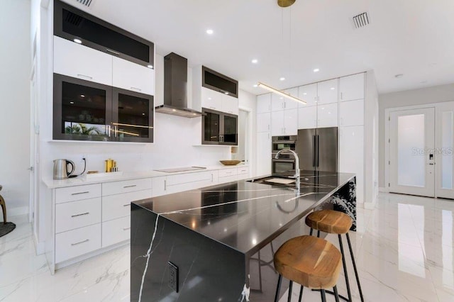 kitchen featuring wall chimney range hood, white cabinetry, stainless steel appliances, and a large island with sink