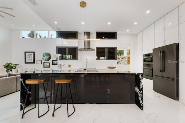 kitchen with wall chimney exhaust hood, a center island with sink, white cabinets, a kitchen bar, and appliances with stainless steel finishes