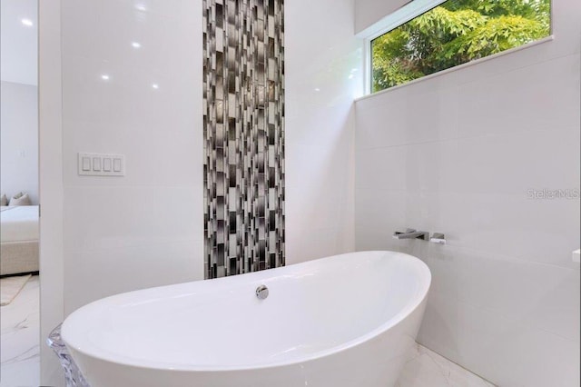 bathroom with a bathing tub, a healthy amount of sunlight, and tile walls