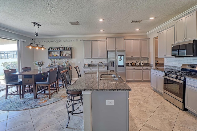 kitchen with stainless steel appliances, a sink, visible vents, dark stone counters, and a kitchen bar