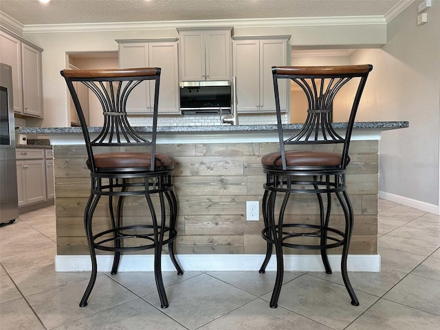 kitchen featuring ornamental molding, a breakfast bar, freestanding refrigerator, and gray cabinetry