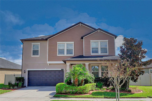 traditional-style house featuring driveway, an attached garage, fence, and stucco siding