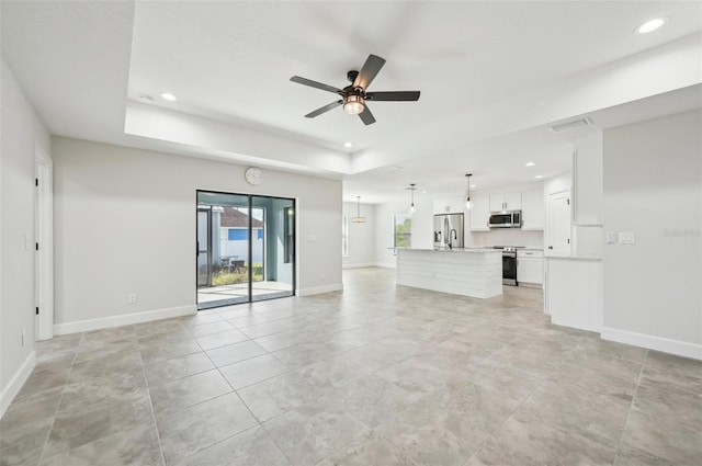 unfurnished living room with ceiling fan, a raised ceiling, and sink