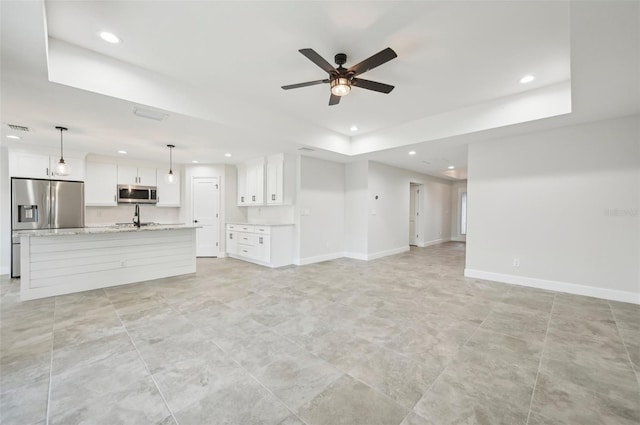 unfurnished living room featuring ceiling fan, sink, and a tray ceiling