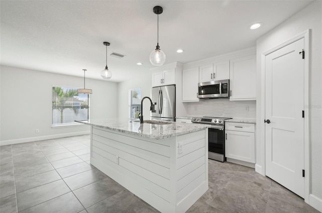 kitchen with light stone countertops, stainless steel appliances, pendant lighting, white cabinetry, and an island with sink