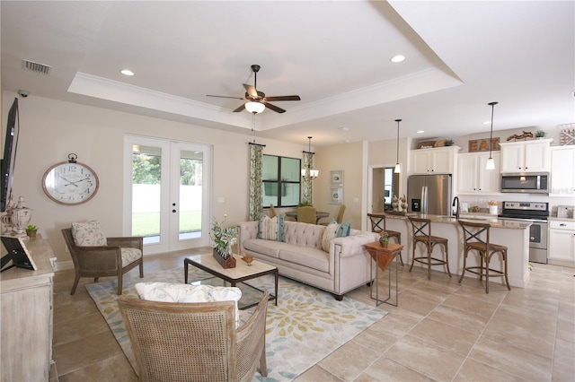 living room with french doors, a tray ceiling, crown molding, light tile patterned floors, and ceiling fan with notable chandelier