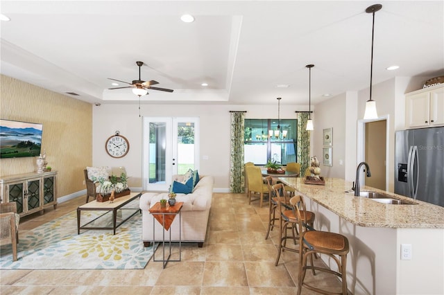 living room featuring sink, ceiling fan with notable chandelier, and a raised ceiling