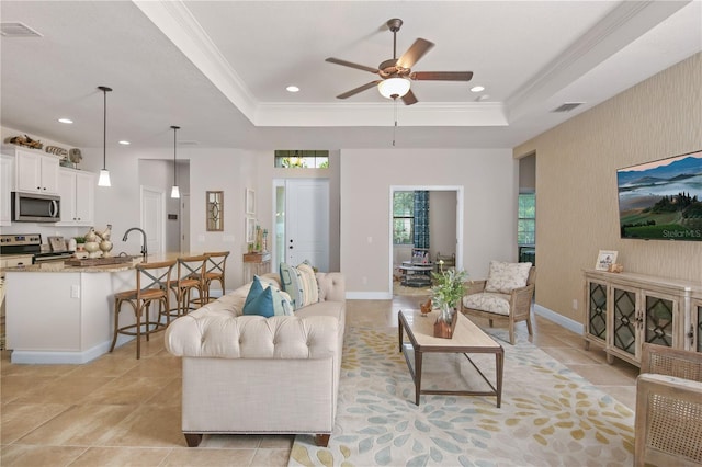 tiled living room featuring sink, ceiling fan, ornamental molding, and a tray ceiling