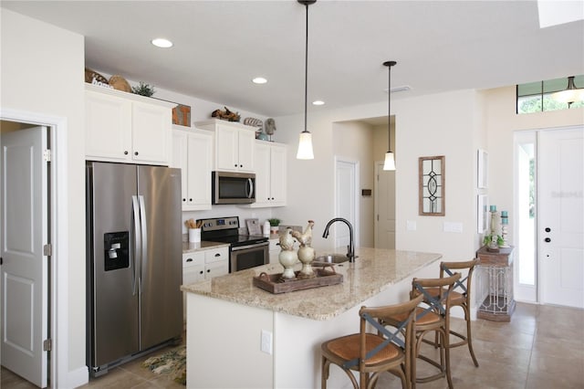 kitchen featuring a breakfast bar area, appliances with stainless steel finishes, an island with sink, white cabinetry, and decorative light fixtures