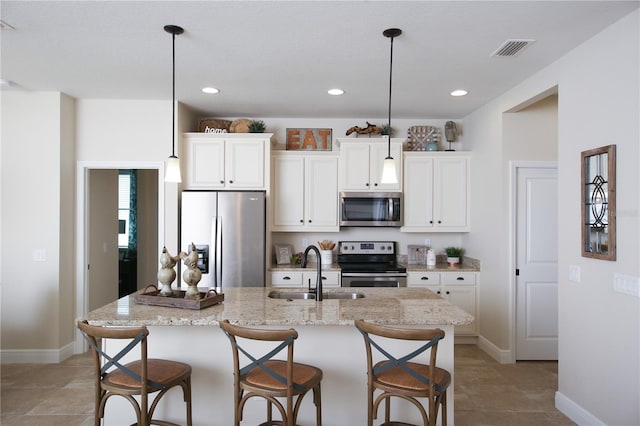 kitchen with appliances with stainless steel finishes, sink, an island with sink, hanging light fixtures, and light stone counters