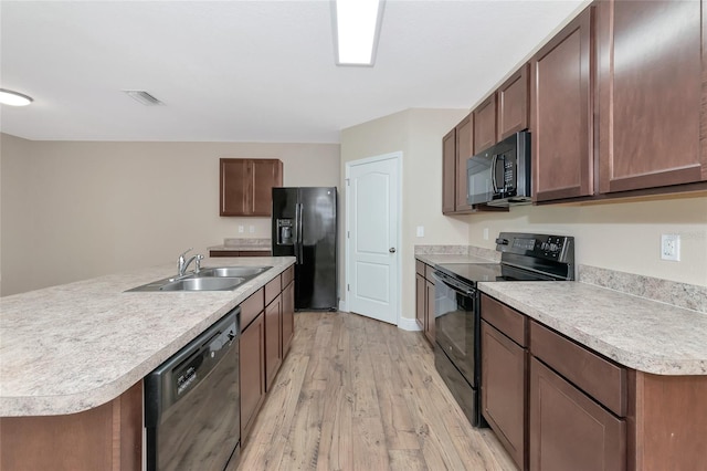 kitchen with light hardwood / wood-style floors, black appliances, sink, and an island with sink