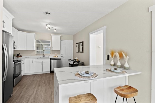 kitchen with a peninsula, a sink, appliances with stainless steel finishes, light stone countertops, and a breakfast bar area