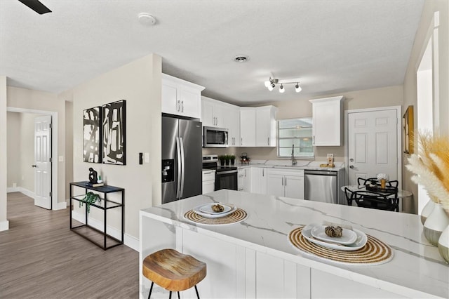 kitchen with kitchen peninsula, stainless steel appliances, hardwood / wood-style floors, white cabinetry, and light stone counters