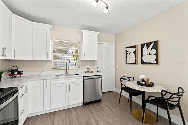 kitchen with light wood-type flooring, stainless steel dishwasher, a sink, and white cabinetry
