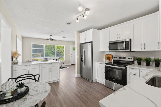 kitchen with white cabinets, stainless steel appliances, light stone counters, and dark hardwood / wood-style floors