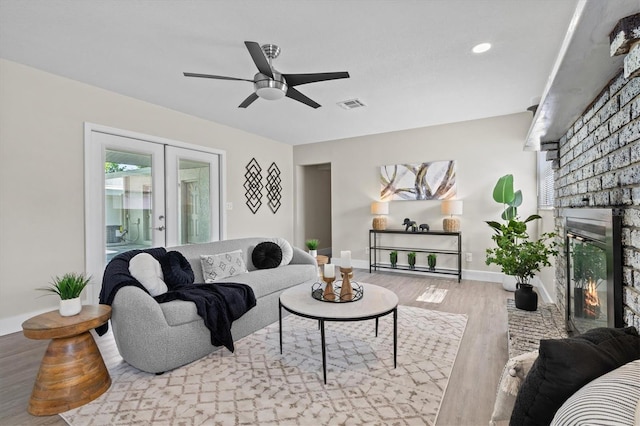 living room with french doors, a brick fireplace, light wood-type flooring, and ceiling fan