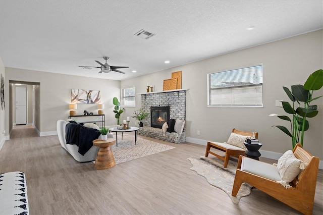 living room featuring a textured ceiling, a stone fireplace, light wood-type flooring, and a healthy amount of sunlight