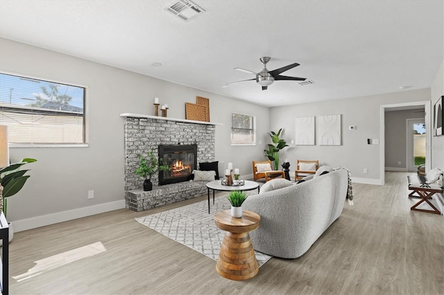 living room with a fireplace, light wood-type flooring, and ceiling fan