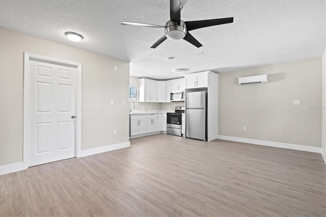 unfurnished living room featuring a wall mounted AC, sink, light wood-type flooring, a textured ceiling, and ceiling fan