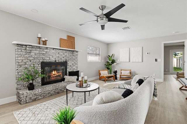 living room with a fireplace, light wood-type flooring, and ceiling fan