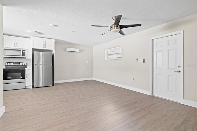 unfurnished living room featuring light hardwood / wood-style floors, a wall unit AC, a textured ceiling, and ceiling fan