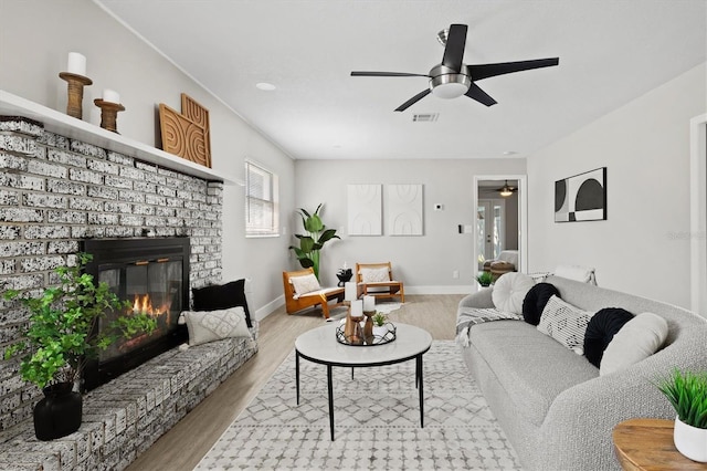 living room featuring ceiling fan, a brick fireplace, and light wood-type flooring