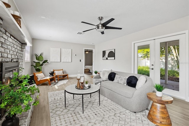 living room with french doors, a fireplace, light wood-type flooring, and ceiling fan