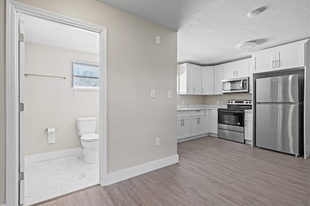 kitchen with light hardwood / wood-style floors, white cabinetry, stainless steel appliances, and a textured ceiling