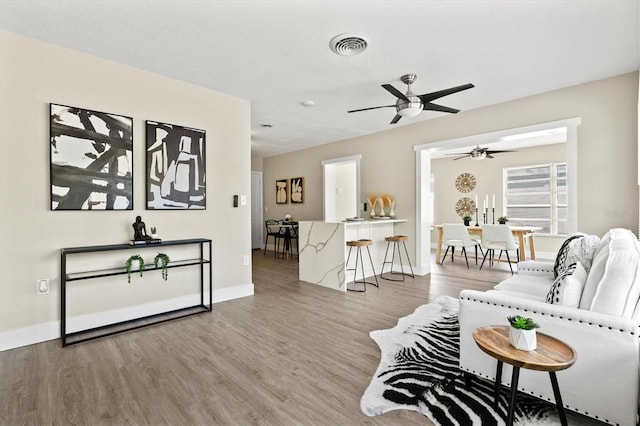 living room featuring visible vents, ceiling fan, baseboards, and wood finished floors
