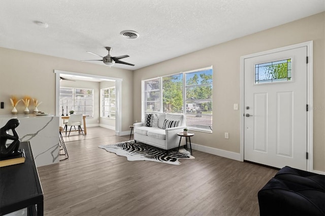 living room with baseboards, a textured ceiling, visible vents, ceiling fan, and wood finished floors