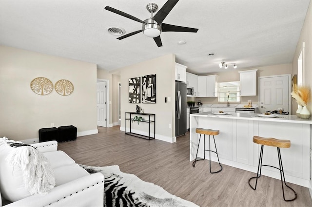 living area featuring visible vents, baseboards, light wood-style flooring, and ceiling fan