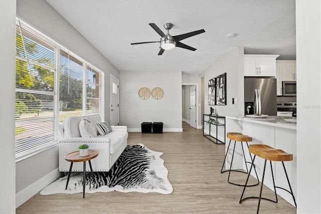 living room with light wood-style floors, baseboards, and a ceiling fan